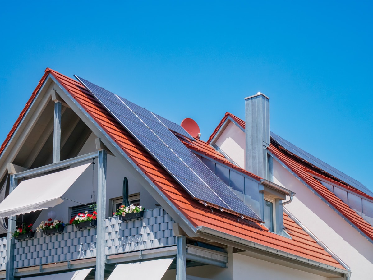 Maison avec panneaux solaires et végétation sous un ciel bleu